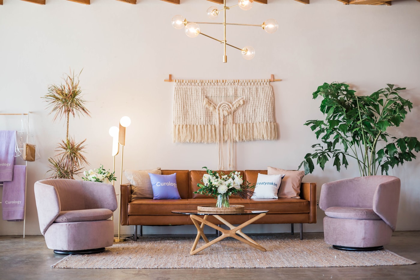 A warm lounge with a tan leather sofa, brass chandelier and blush occasional chairs