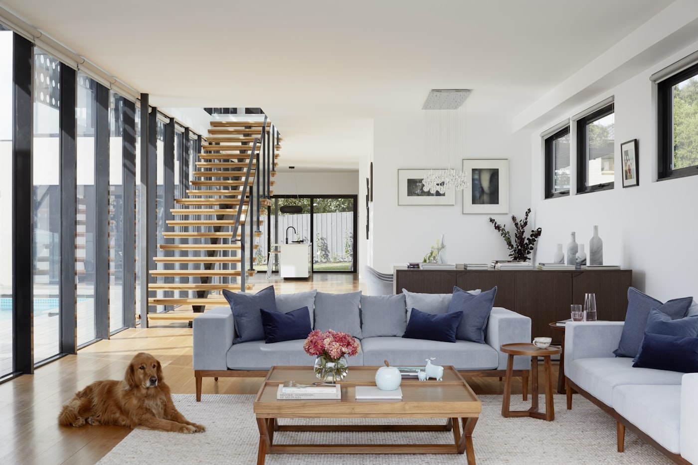 A double-height villa living room with a staircase, navy accents and a pale timber floor